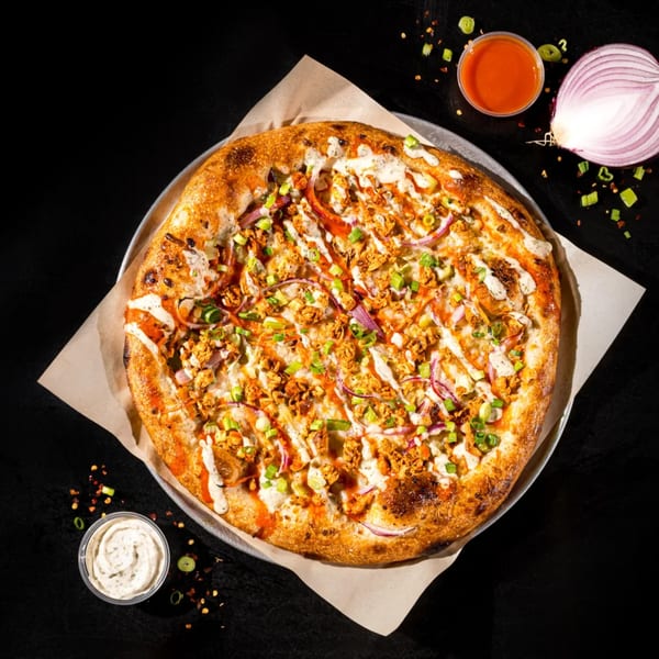 Earthly's vegan pizza, topped with plant-based chicken, red onion, green onion, and white and red sauces.