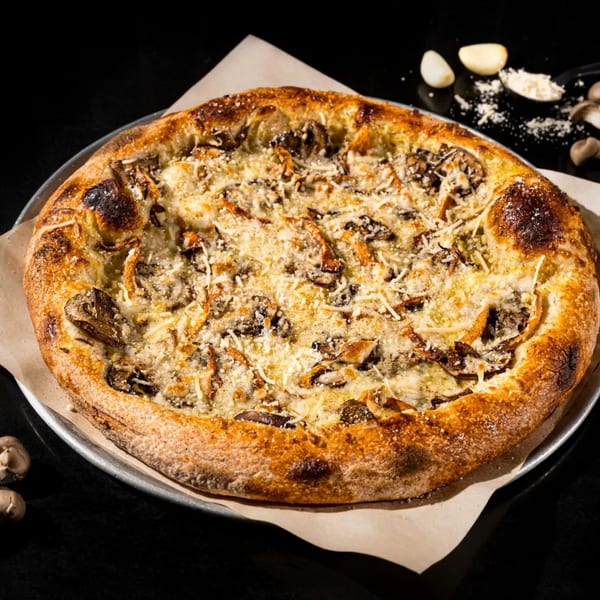 Vegan mushroom pizza with white sauce and cheese on a metal pan with garlic and mushrooms.