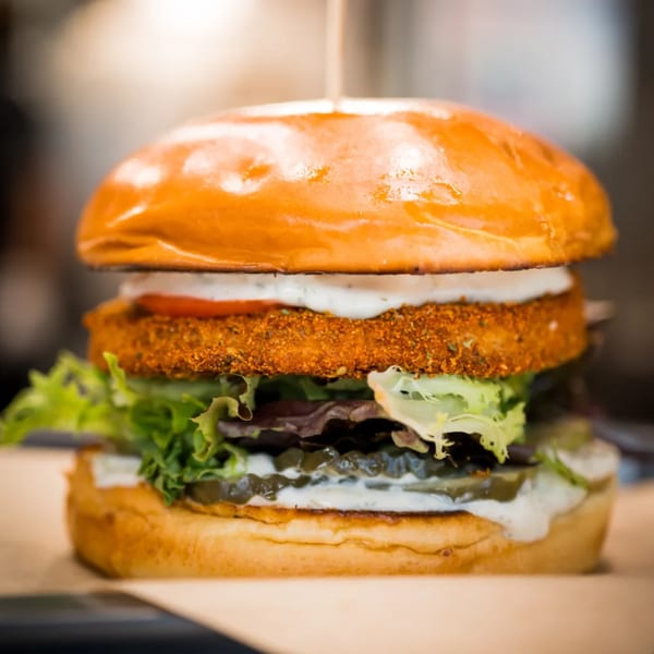 Close-up of Earthly's vegan burger with a crispy patty, lettuce, tomato, pickles, and creamy sauce.