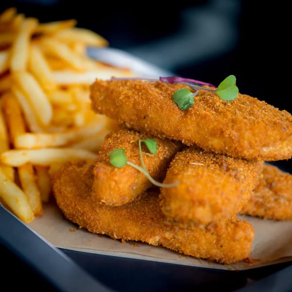 Crispy vegan chicken tenders with fries, garnished with microgreens, served on a tray.