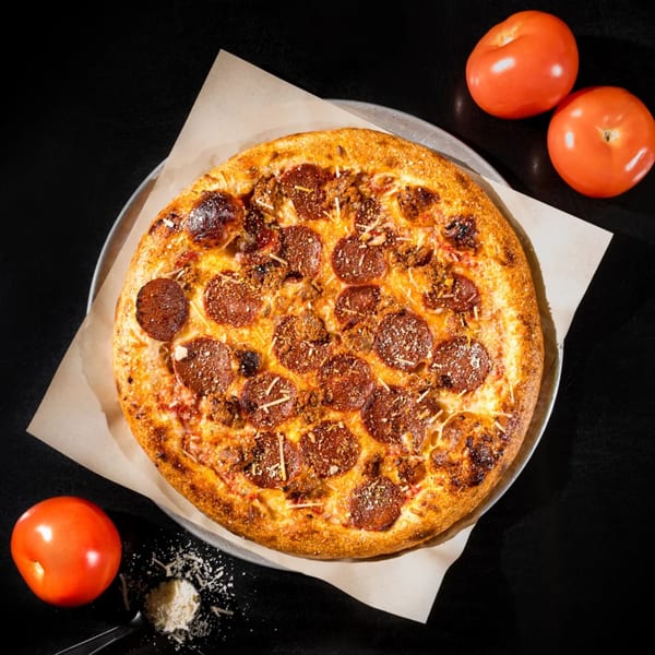 Vegan pepperoni and sausage pizza on a metal pan with tomatoes and parmesan on a dark surface.